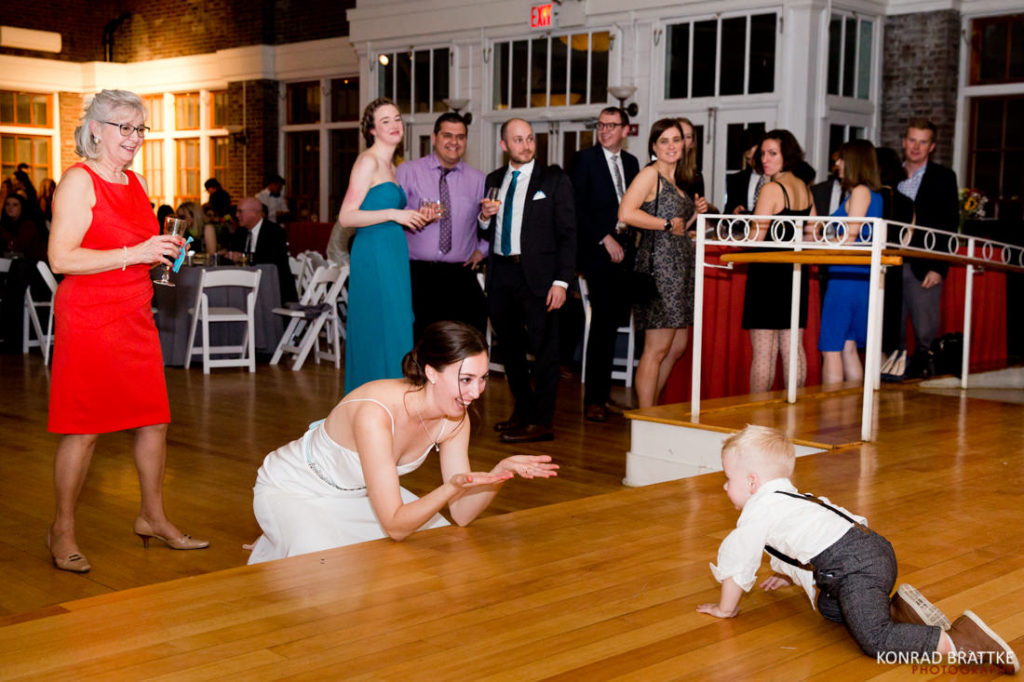 A bride and groom at a wedding with a baby on the floor.