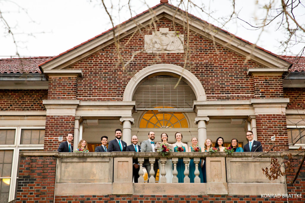 A group of bridesmaids and groomsmen standing on the balcony of the Prospect Park Picnic house.