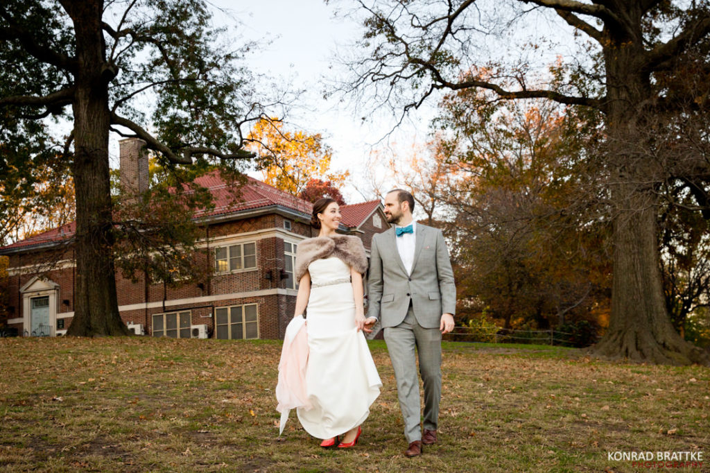 A beautiful bride and a dashing groom holding hands in front of a large house, capturing the essence of their Prospect Park wedding.