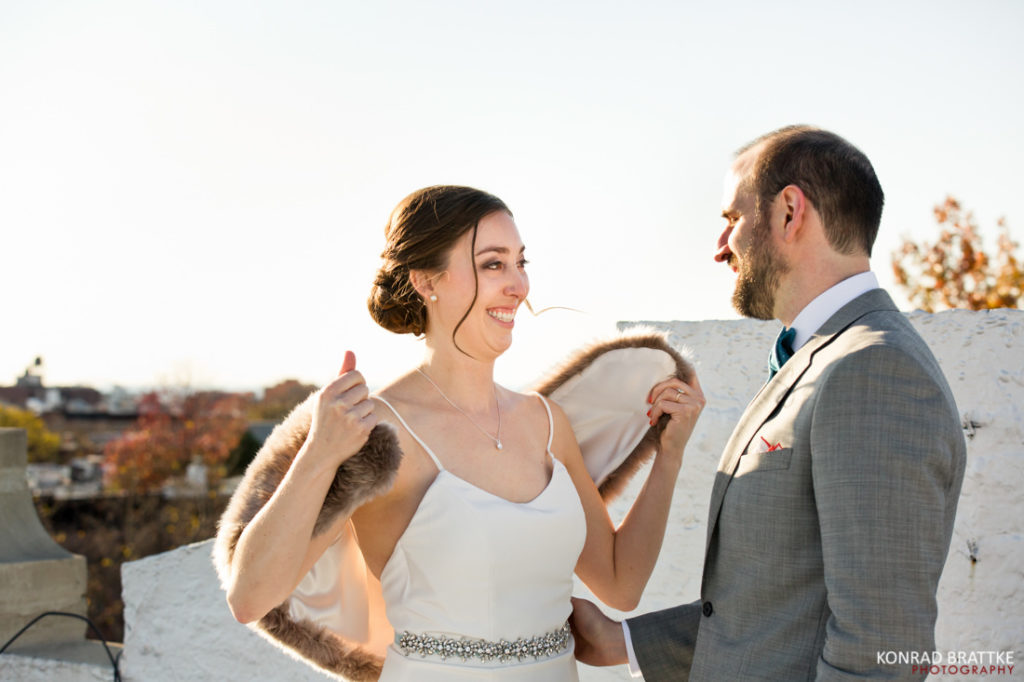 A couple, beautifully dressed in wedding attire, sharing a heartfelt gaze amidst a picturesque rooftop view.