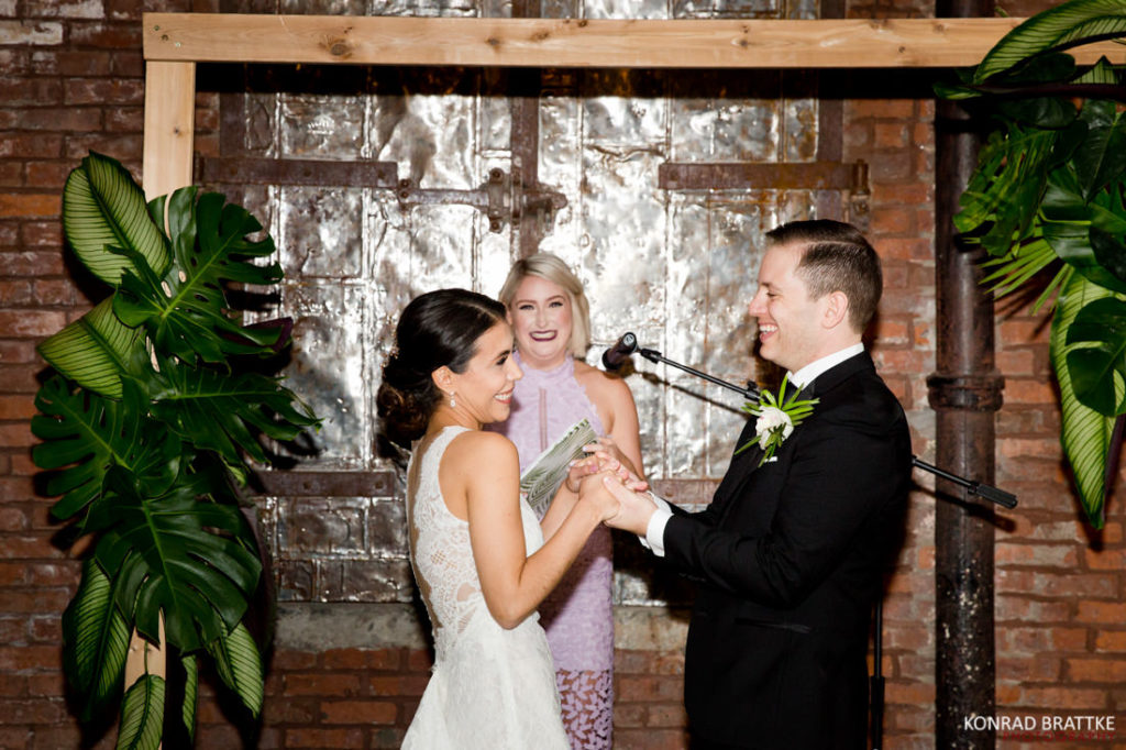 A bride and groom exchange vows in front of the 26 Bridge, a stunning brick wall backdrop.