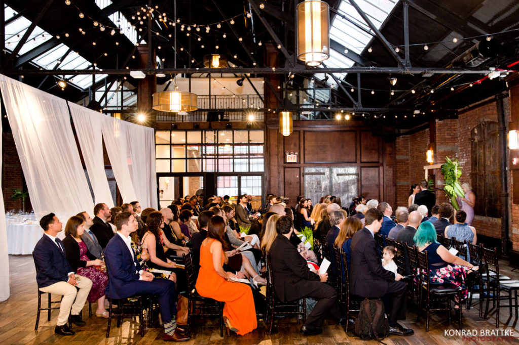 A wedding ceremony at the 26 Bridge, a large room with people sitting in chairs.