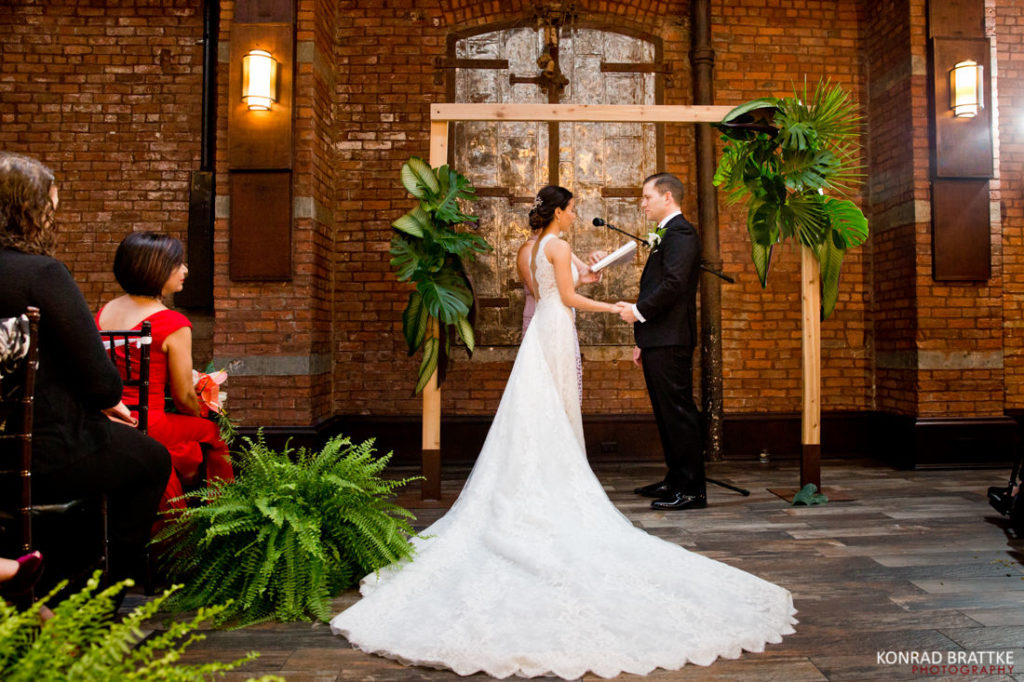 A bride and groom exchange vows at 26 Bridge, a brick building.