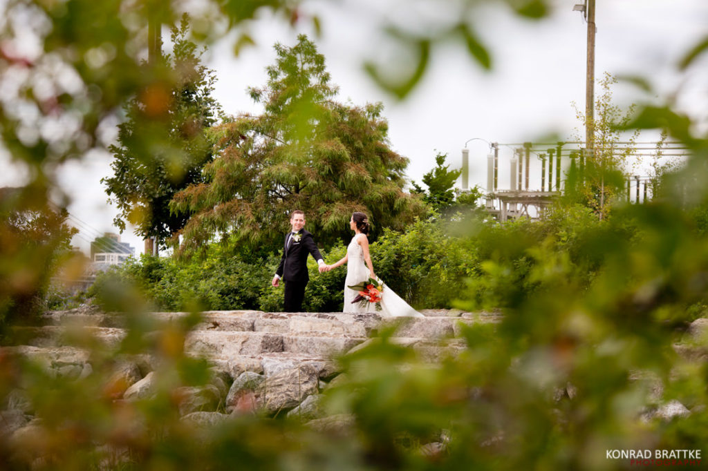 A bride and groom standing on a rock in the woods, by a 26 Bridge.
