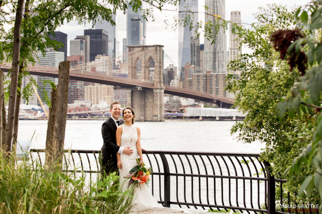 A bride and groom pose for a photo in front of the Brooklyn Bridge.