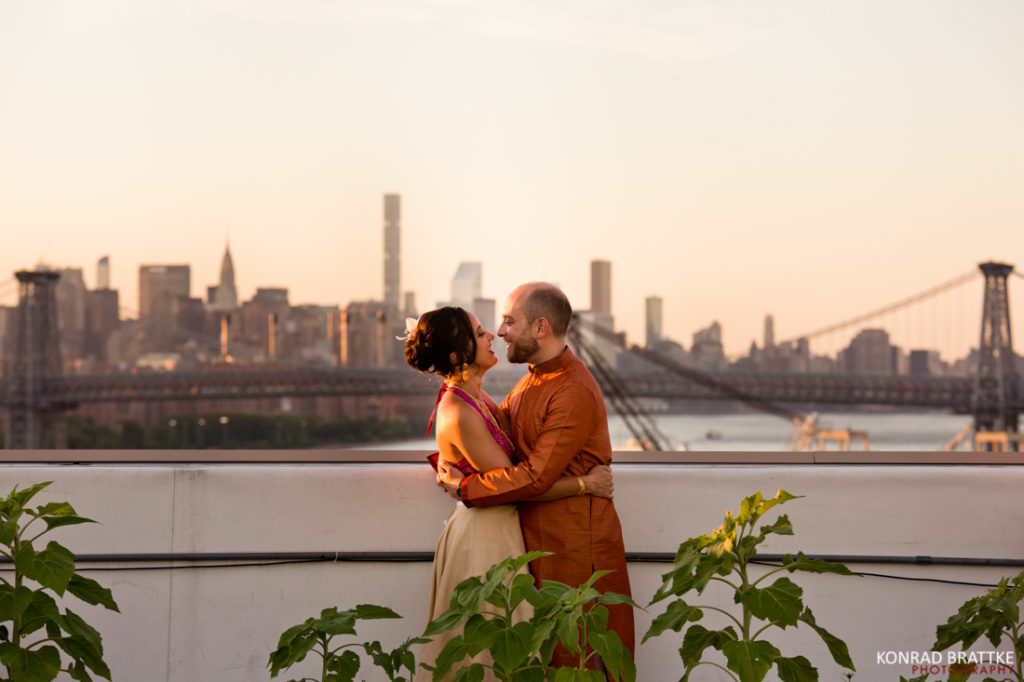 A wedding couple embracing on a rooftop overlooking the Brooklyn Bridge during a Brooklyn Grange wedding.