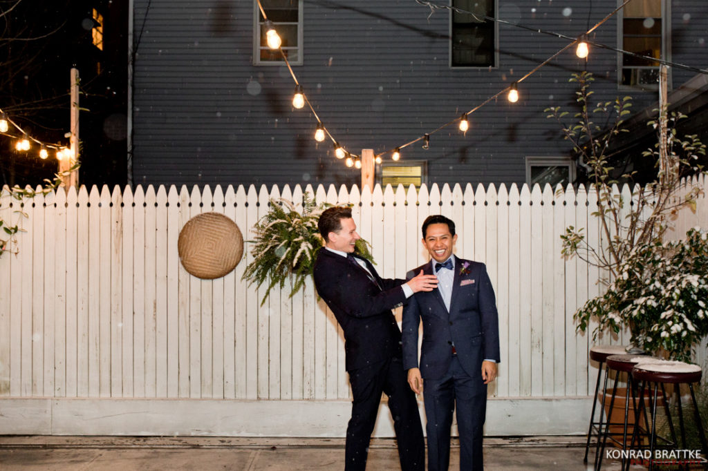 Two grooms standing next to each other in front of a fence at Le Fanfare.