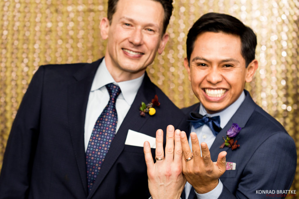 Two grooms posing for a photo at Le Fanfare with their wedding rings.