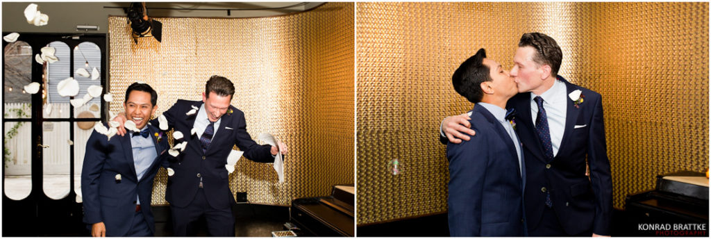 Two grooms, sharing an affectionate moment while standing in front of a shimmering gold wall at their venue.