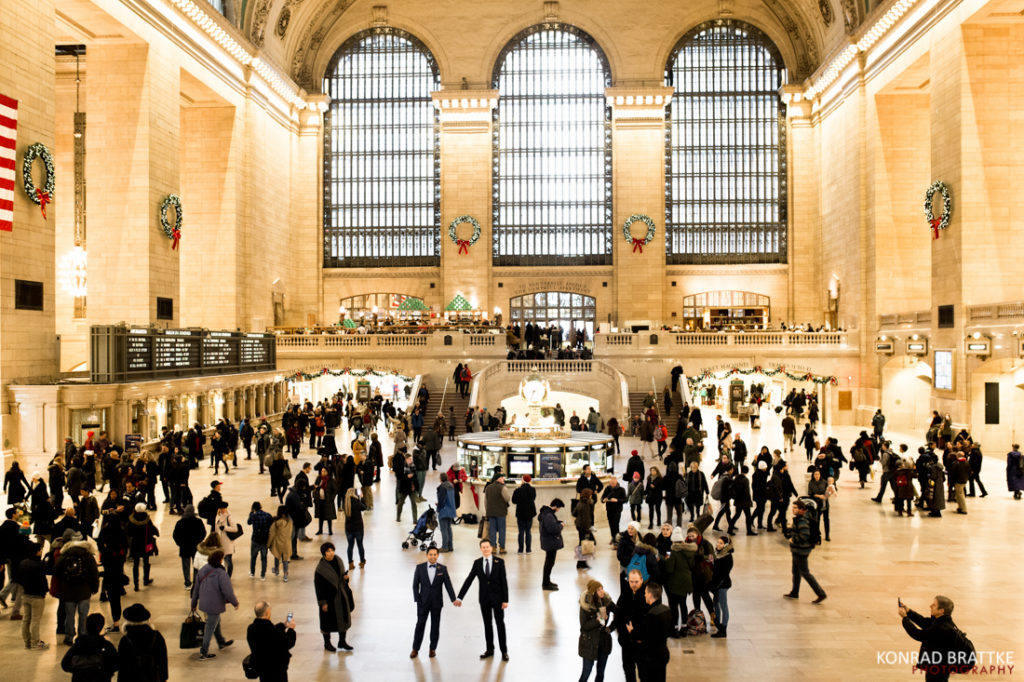 Two grooms standing in the middle Grand Central Station in New York City.