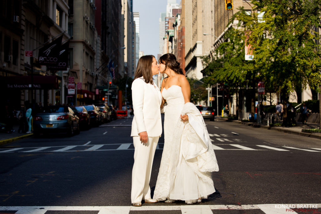 A Manhattan bride and bride kiss in the middle of a city street.