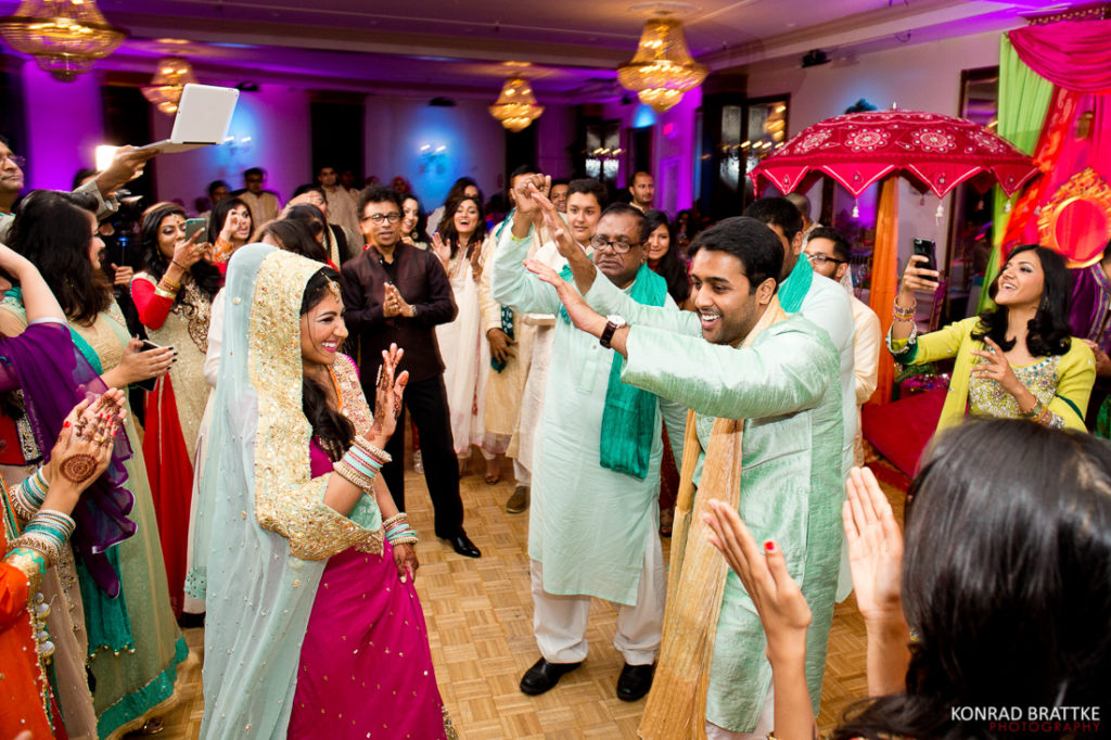 A bride and groom dancing at a mehndi ceremony during an Indian wedding reception.