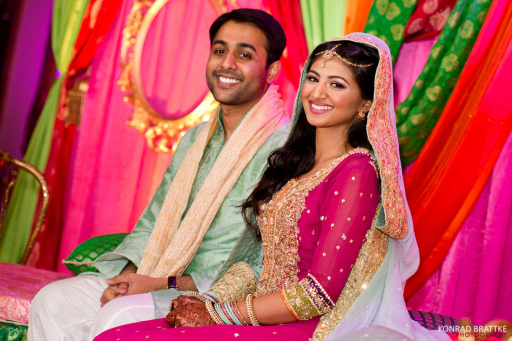 A mehndi bride and groom sitting in front of colorful decorations at Antuns.