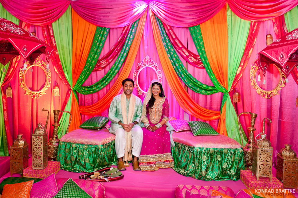 A couple sits on a colorful bed at a Mehndi celebration in an Indian wedding at Antuns.