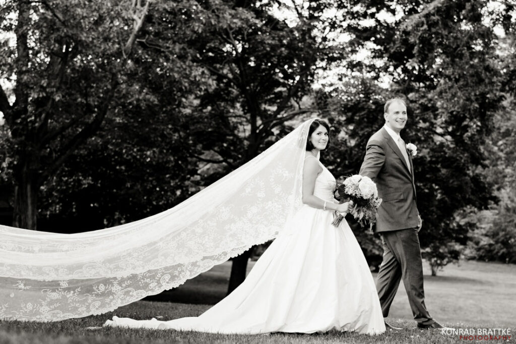 Black and white photo of a bride and groom holding a veil.