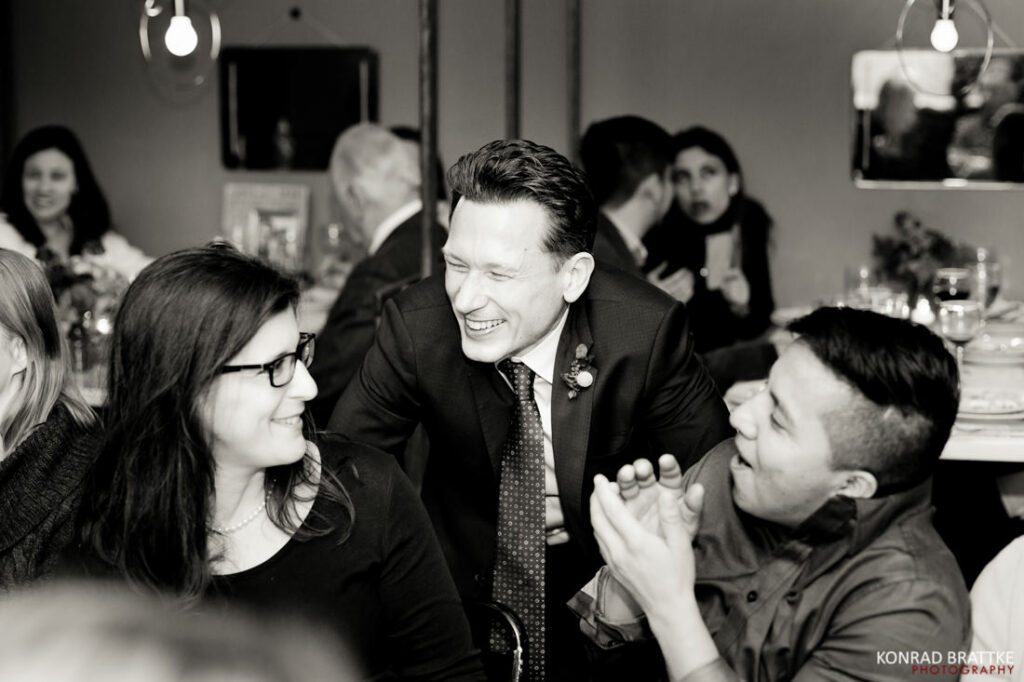 A black and white photo of a group of people laughing at a wedding reception.
