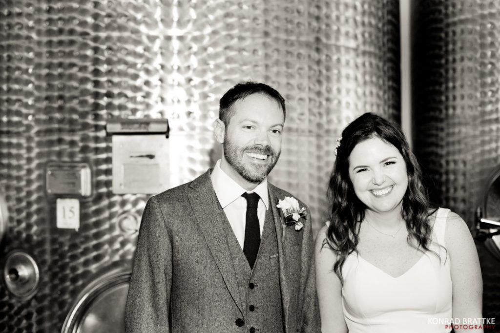 A bride and groom standing in front of wine barrels at Brooklyn Winery.