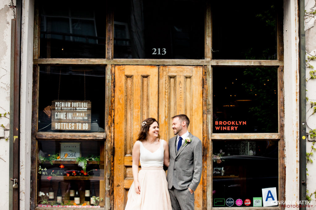A bride and groom posing elegantly in front of a wooden door at the Brooklyn Winery.