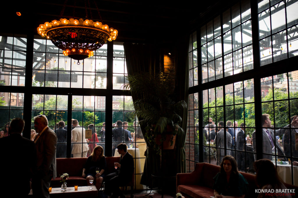 A group of people standing in a room with large windows at the Bowery Hotel wedding.