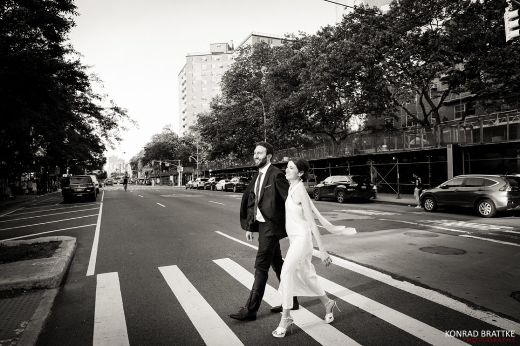 A black and white photo of a bride and groom crossing a street.