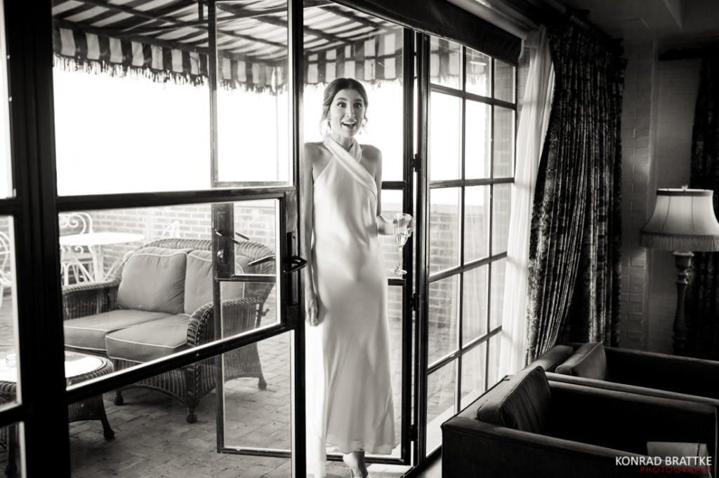 A bride in a white dress standing in front of a window.