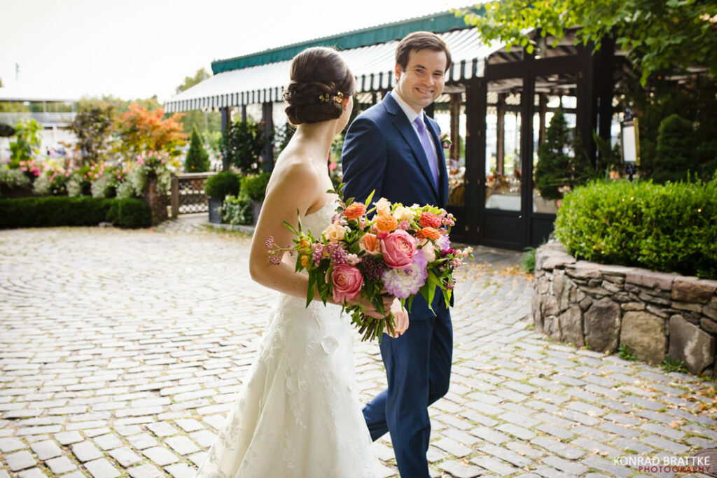 A bride and groom walking down a cobblestone walkway by river cafe.