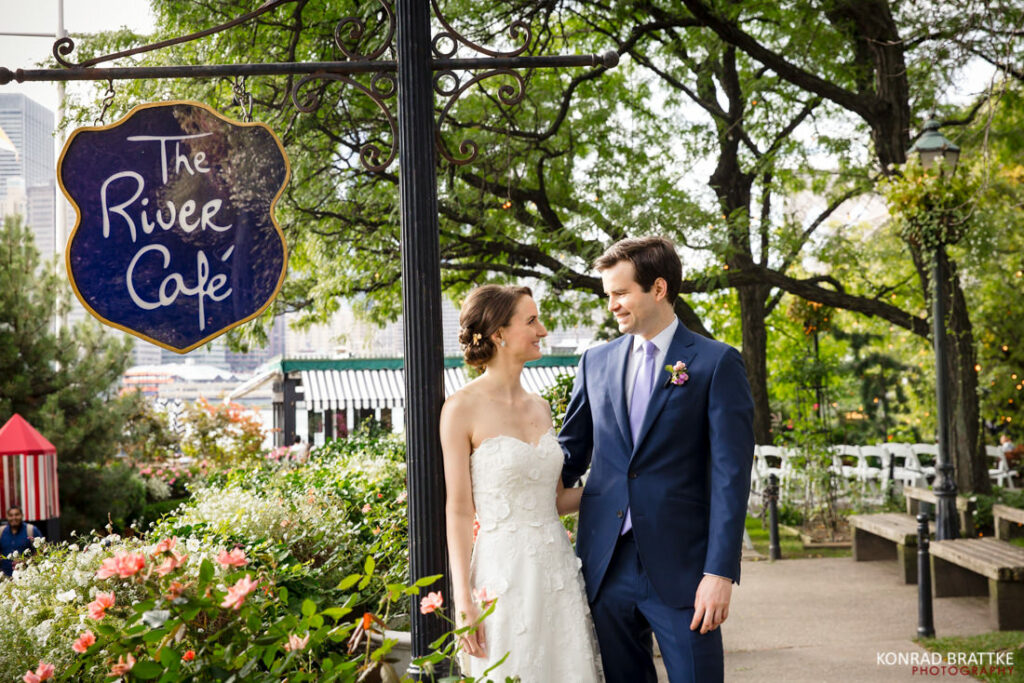 A bride and groom standing in front of the river cafe sign.