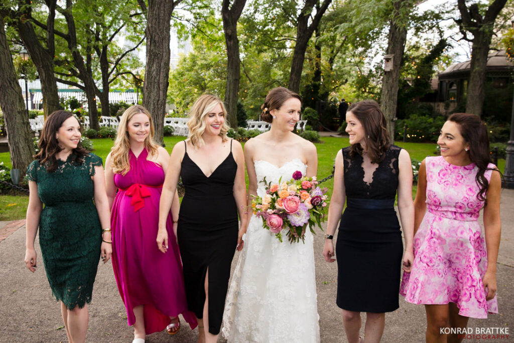 A bride and her bridesmaids are walking in a park near the river cafe.