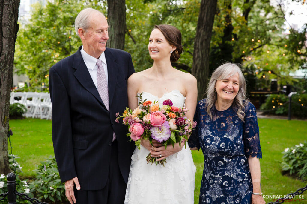 A bride and her parents pose for a photo at river cafe park.
