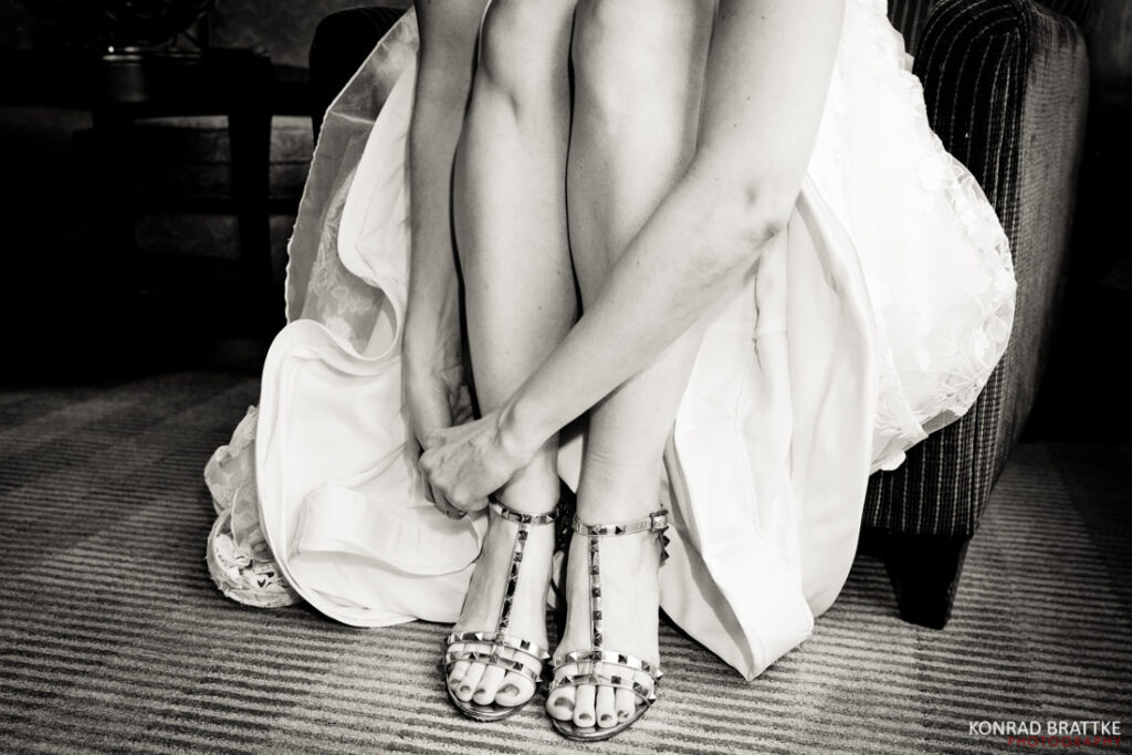 A black and white photo of a bride tying her shoes.