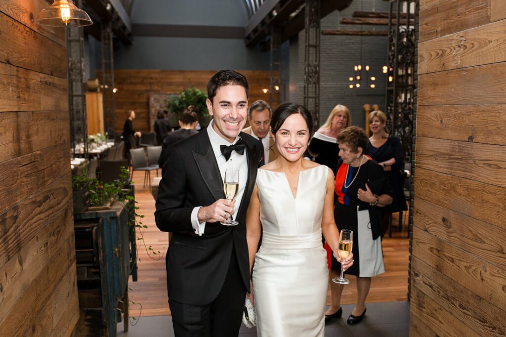 A bride and groom holding champagne glasses in a hallway at The Milling Room.