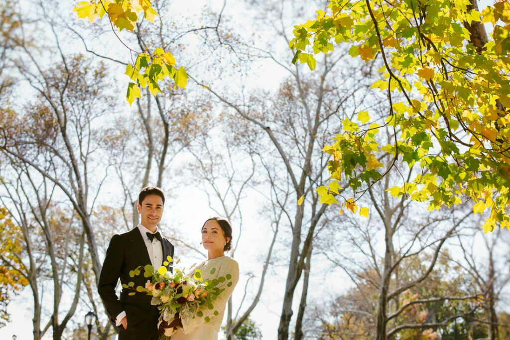 A bride and groom standing in central park with trees in the background.