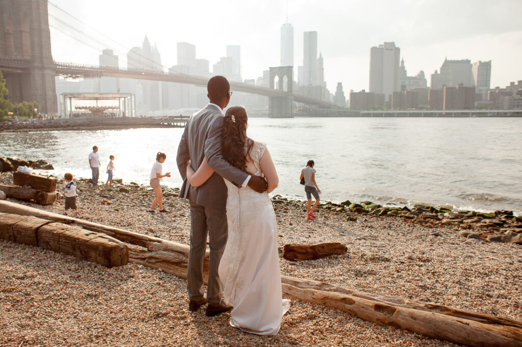 A bride and groom standing in front of the Brooklyn Bridge.