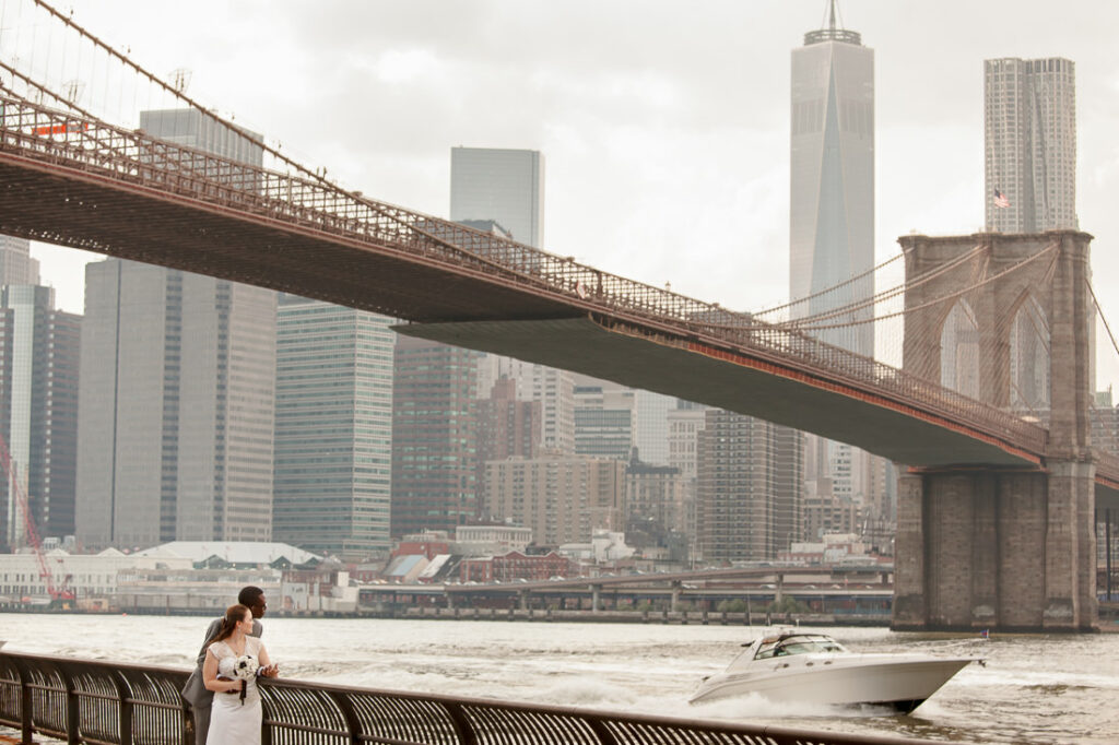 A bride and groom posing elegantly in front of the Brooklyn Bridge.