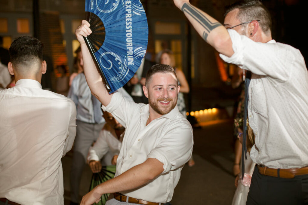 A man is holding a blue fan at the New York Botanical Garden during a wedding reception.