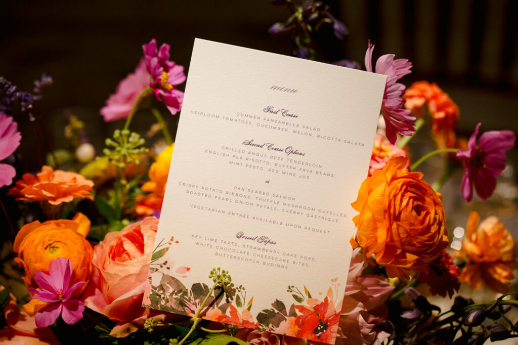 A wedding menu is sitting on a table at the New York Botanical Garden, surrounded by flowers.
