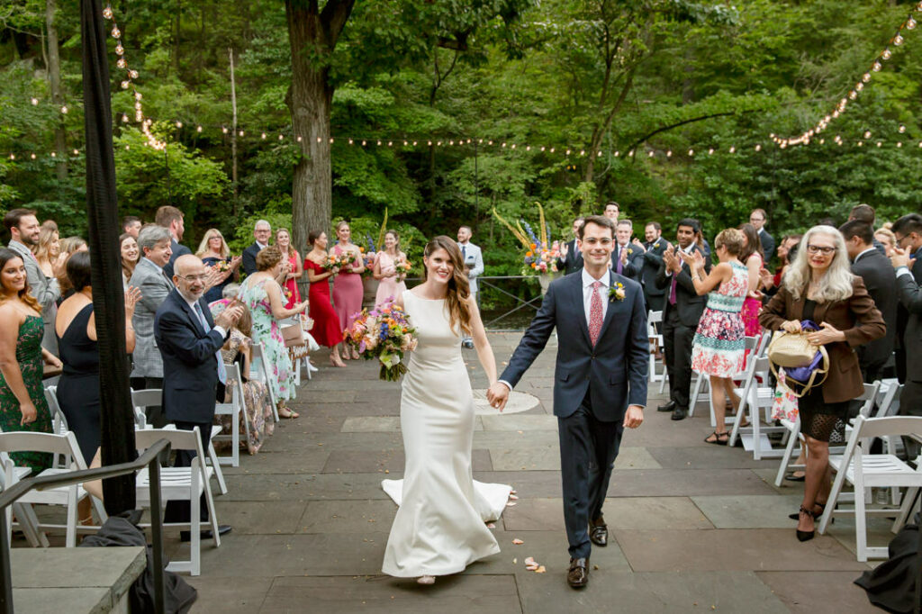 A bride and groom walking down the aisle at an outdoor wedding at the New York Botanical Garden.