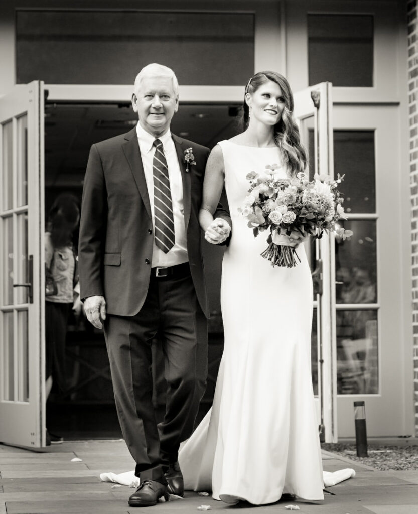 A black and white photo of a bride and her father walking down the aisle at the New York Botanical Garden.