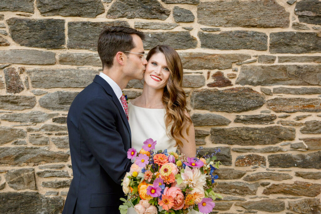 A bride and groom embracing in front of a stone wall at the New York Botanical Garden.