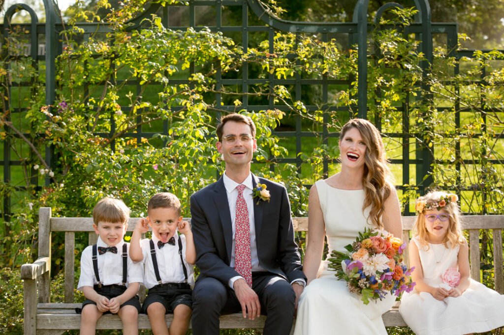 A bride and groom sitting on a bench in the New York Botanical Garden with their children.