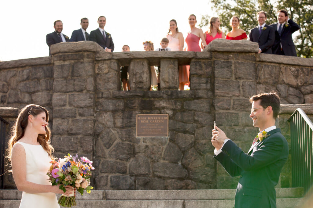 A bride and groom taking a picture at the New York Botanical Garden in front of a stone wall.