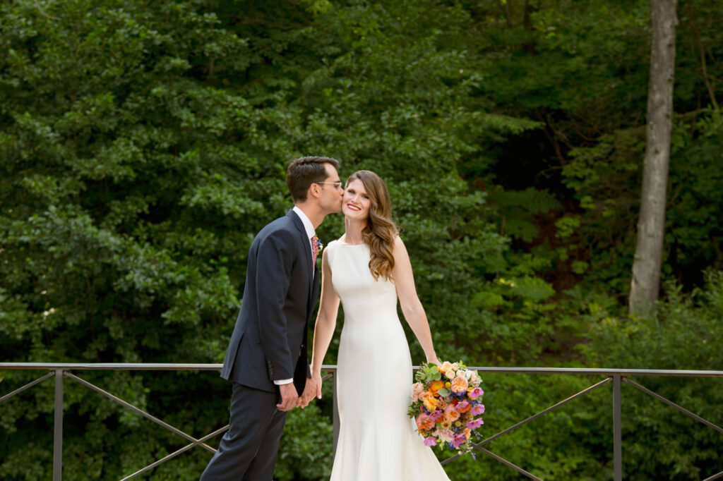 A bride and groom kissing on a bridge in the New York Botanical Garden.