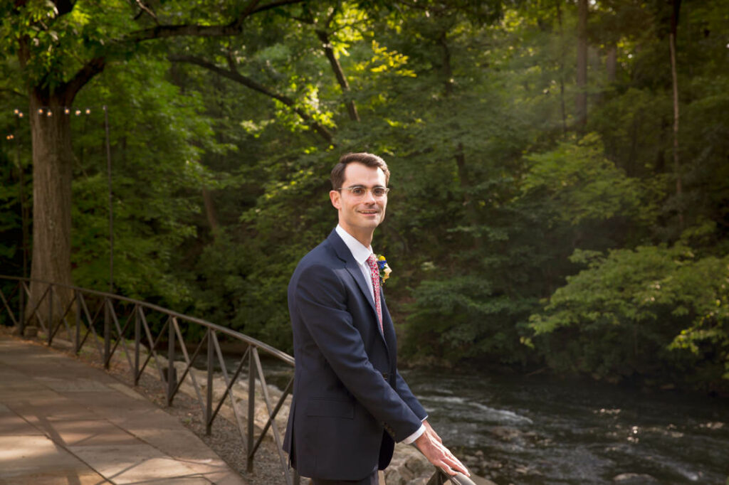 A man in a suit standing next to a river at the New York Botanical Garden.