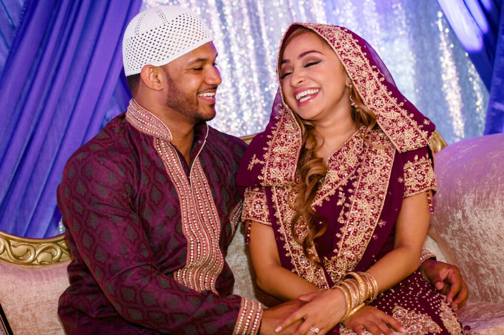 A man and woman dressed in traditional Islamic attire are smiling during their nikah ceremony.