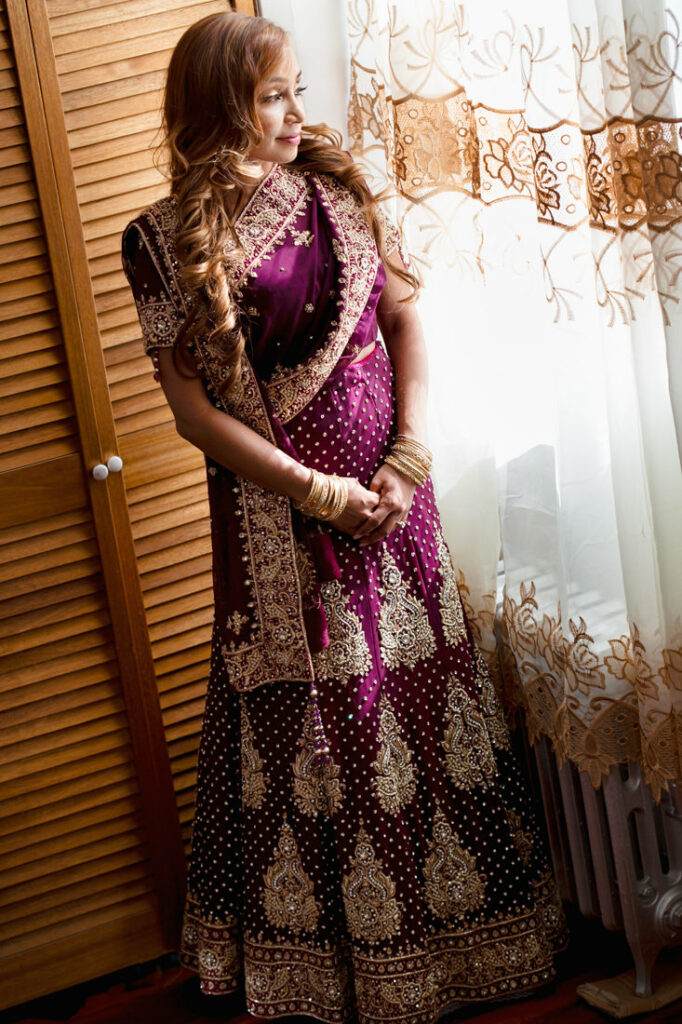 A woman in a purple lehenga posing in front of a window for her nikah ceremony.