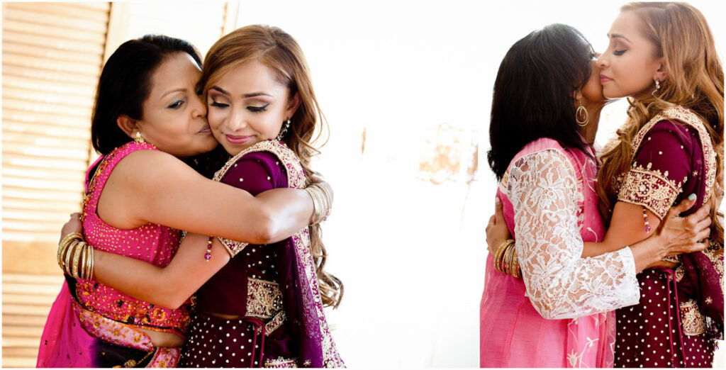 Two women wearing pink saris embrace each other.