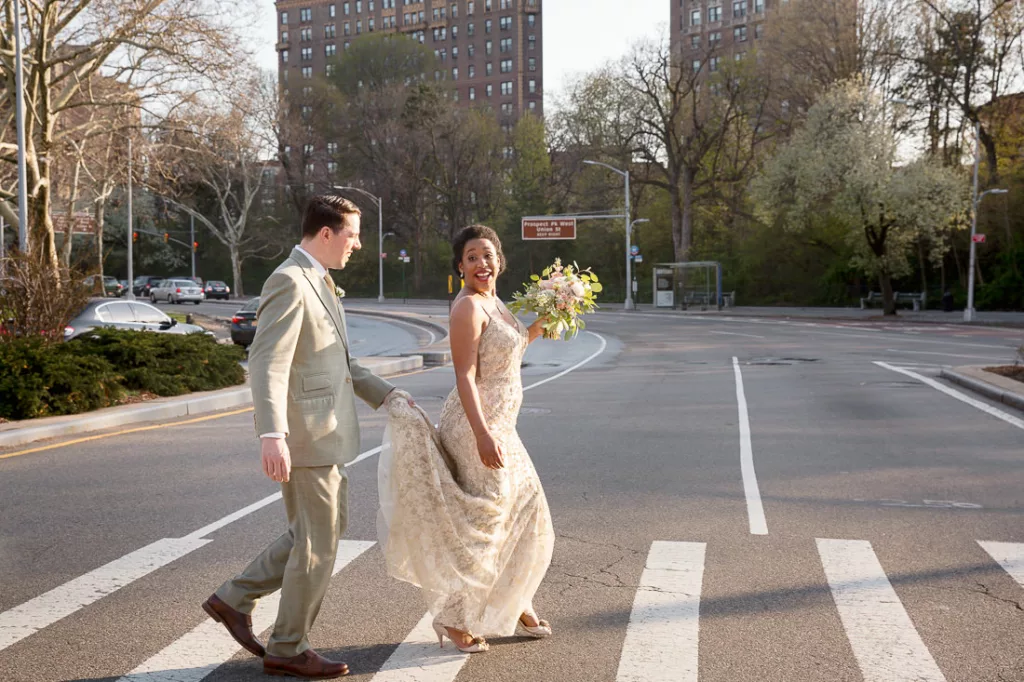 A bride and groom cross the street in front of a building in New York.