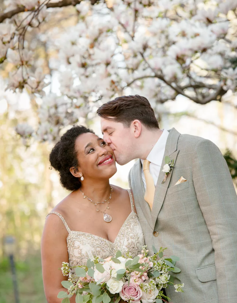 A bride and groom kiss under a cherry blossom tree in Brooklyn, NY.