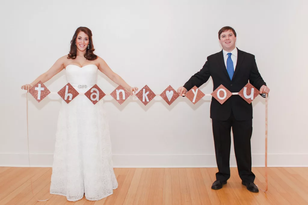 A bride and groom holding up a thank you banner at their wedding at VisArts.