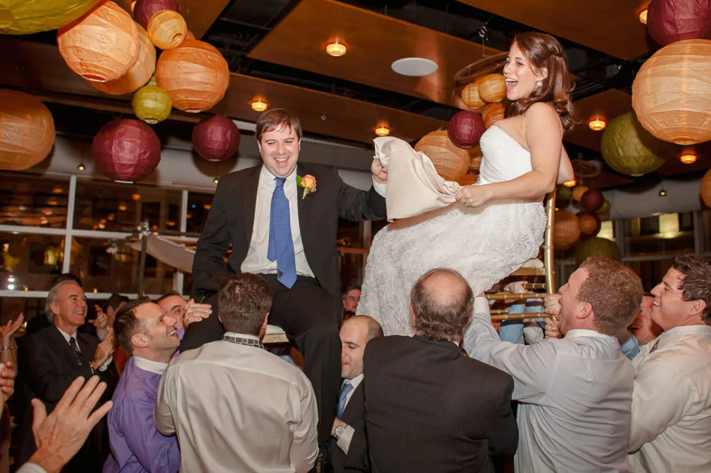 A bride and groom are being carried up on a chair at their wedding at VisArts.